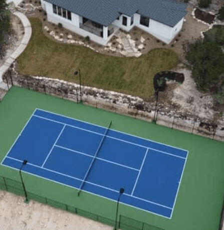 Aerial view of a residential tennis court, seamlessly integrated into the property with well-defined boundaries and a smooth playing area.