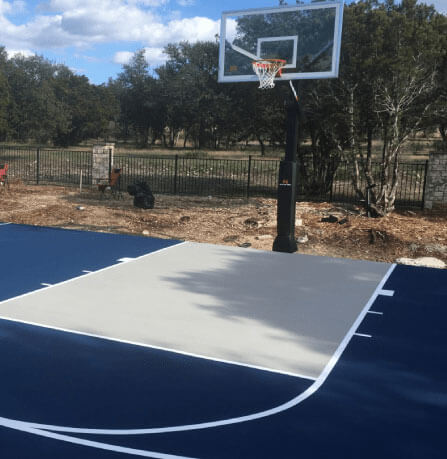 Backyard half-court basketball setup with professional surfacing, adjustable hoop, and clear court markings for private play.
